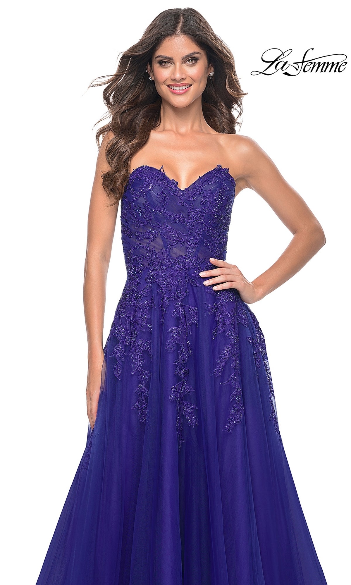A woman stands smiling against a white background, wearing the La Femme Lace-Up Long Sweetheart Prom Dress 32304 in royal blue with lace details. The